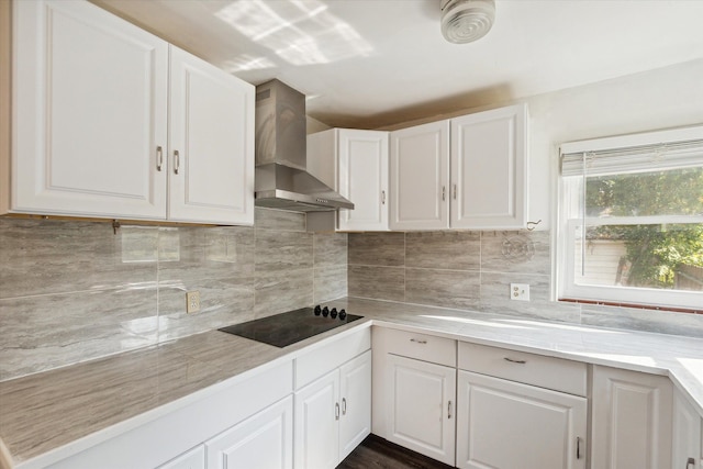 kitchen featuring white cabinets, backsplash, black electric cooktop, and wall chimney range hood