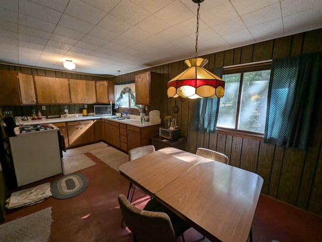 kitchen with pendant lighting, wood walls, white range oven, and sink