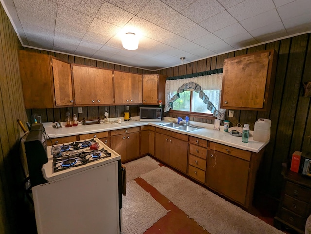 kitchen featuring white range with gas stovetop, sink, and wood walls