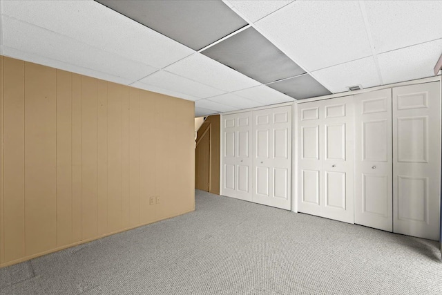 basement with carpet flooring, a paneled ceiling, and wood walls