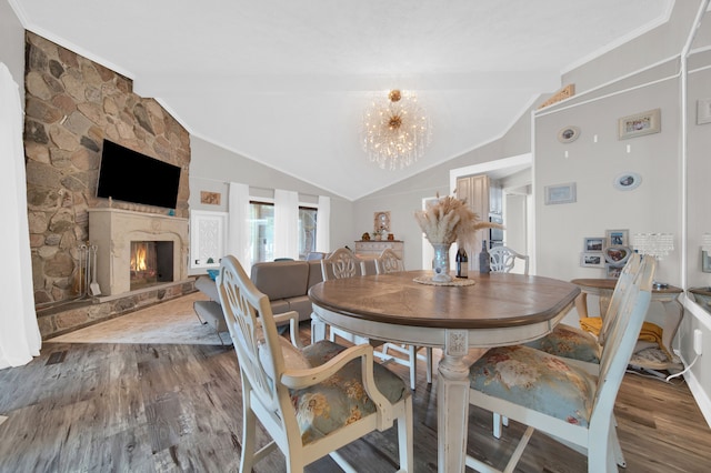 dining area featuring a notable chandelier, vaulted ceiling with beams, a stone fireplace, and wood-type flooring