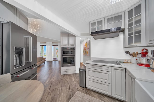 kitchen with gray cabinetry, hardwood / wood-style flooring, light stone countertops, a notable chandelier, and stainless steel appliances