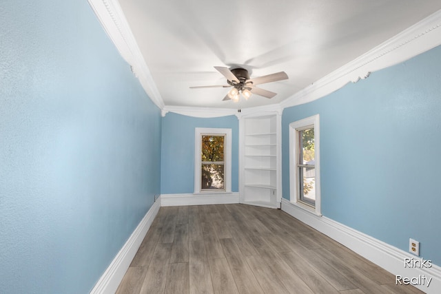 empty room with built in shelves, crown molding, ceiling fan, and hardwood / wood-style flooring