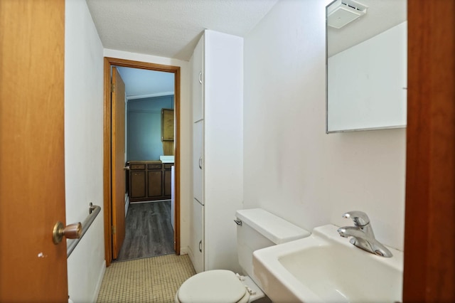 bathroom with hardwood / wood-style flooring, toilet, sink, and a textured ceiling