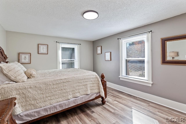 bedroom featuring multiple windows, light hardwood / wood-style floors, and a textured ceiling