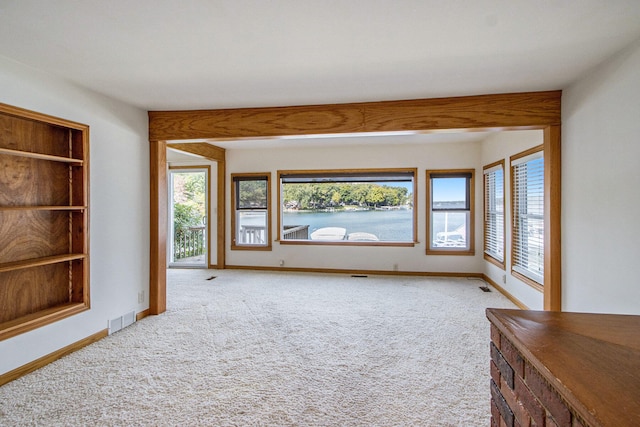 unfurnished living room with a water view, a wealth of natural light, and carpet floors