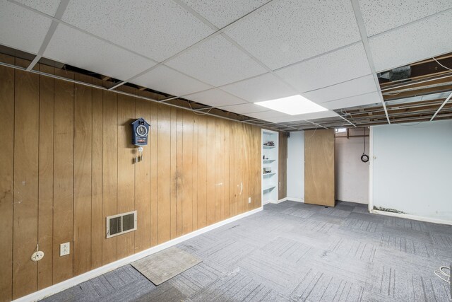 basement featuring carpet, a paneled ceiling, and wooden walls