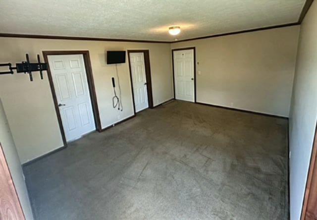 unfurnished room featuring crown molding, a textured ceiling, and dark colored carpet