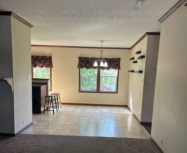 spare room with light carpet, ornamental molding, a textured ceiling, and a notable chandelier