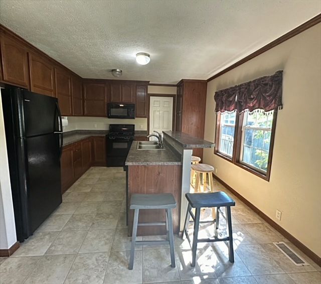 kitchen with a breakfast bar, crown molding, sink, black appliances, and a center island with sink