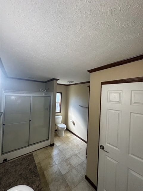 bathroom with a textured ceiling, toilet, walk in shower, and crown molding