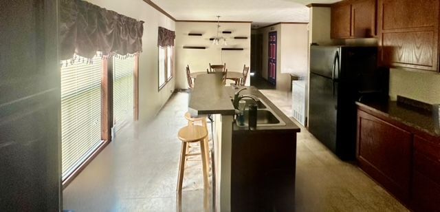 kitchen featuring black fridge, sink, ornamental molding, an island with sink, and a breakfast bar area