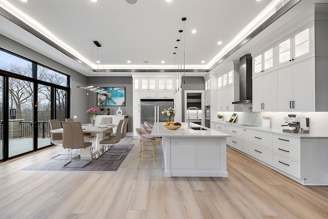 kitchen featuring pendant lighting, white cabinets, wall chimney range hood, sink, and a large island