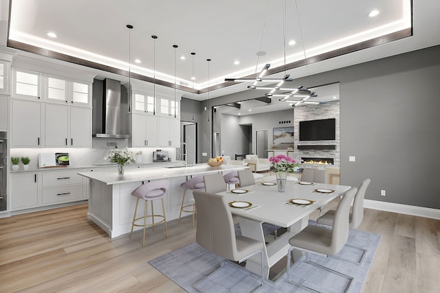 dining space featuring sink, light wood-type flooring, a tray ceiling, and a large fireplace