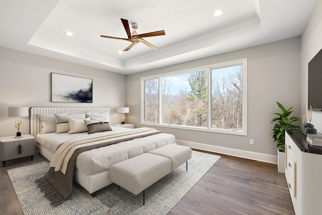 bedroom with ornamental molding, dark hardwood / wood-style floors, ceiling fan, and a tray ceiling