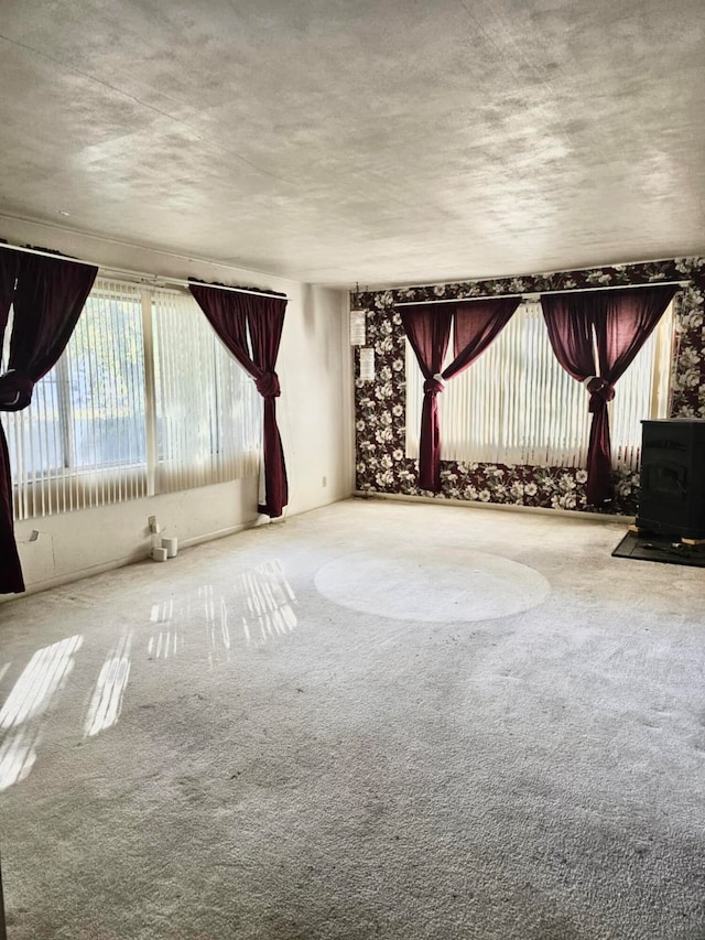 carpeted spare room with a wood stove and a textured ceiling