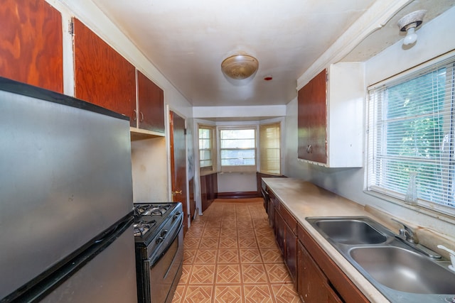 kitchen featuring black gas range oven, stainless steel refrigerator, and sink