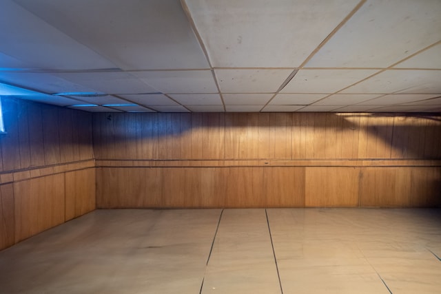 basement featuring a drop ceiling and wooden walls