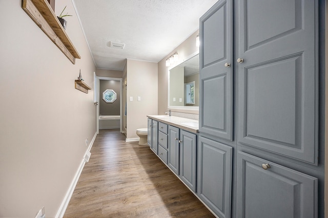 bathroom with wood finished floors, double vanity, baseboards, toilet, and visible vents
