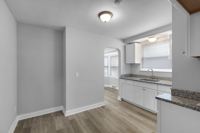 kitchen with white cabinetry, sink, stone counters, and light hardwood / wood-style flooring