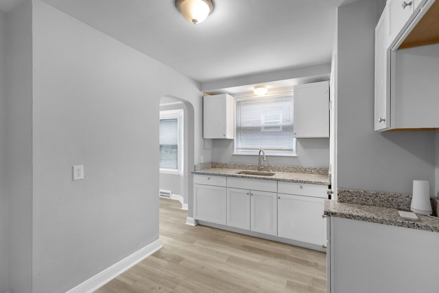 kitchen featuring white cabinets, light wood-type flooring, light stone counters, and sink