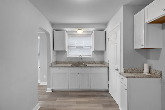 kitchen with light stone counters, light hardwood / wood-style flooring, white cabinetry, and sink