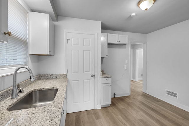 kitchen with light stone countertops, white cabinetry, sink, and light wood-type flooring