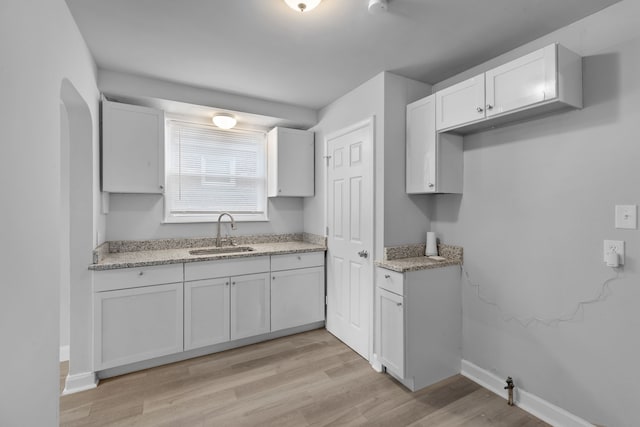 kitchen with light stone countertops, sink, white cabinets, and light hardwood / wood-style floors