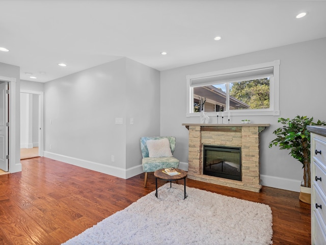 sitting room with a stone fireplace and dark wood-type flooring