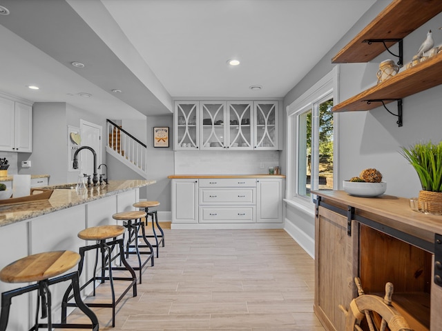 kitchen with light stone countertops, light wood-type flooring, sink, white cabinets, and a breakfast bar area