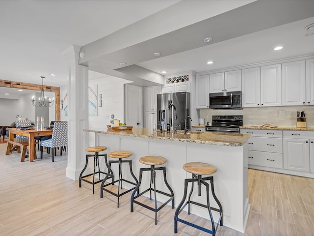 kitchen with an inviting chandelier, light hardwood / wood-style flooring, pendant lighting, white cabinets, and appliances with stainless steel finishes