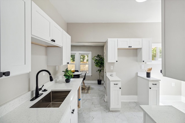 kitchen with light stone counters, white cabinetry, and sink