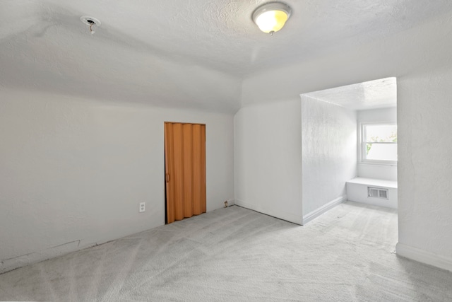 additional living space featuring light carpet and a textured ceiling