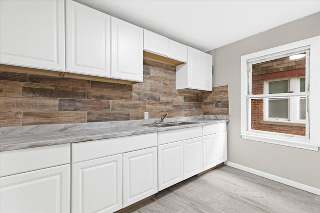 kitchen featuring light stone counters, white cabinetry, sink, and tasteful backsplash