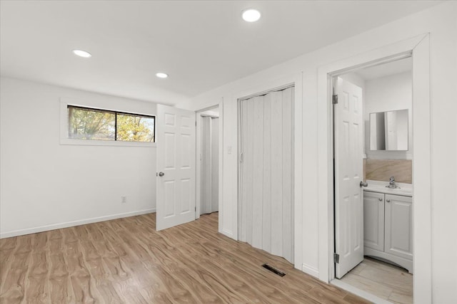 unfurnished bedroom featuring connected bathroom, a closet, light hardwood / wood-style floors, and sink