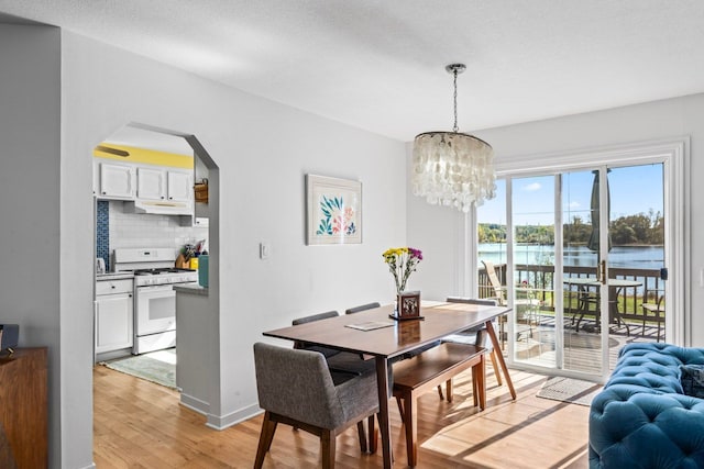 dining area featuring a textured ceiling, light wood-type flooring, a water view, and a notable chandelier