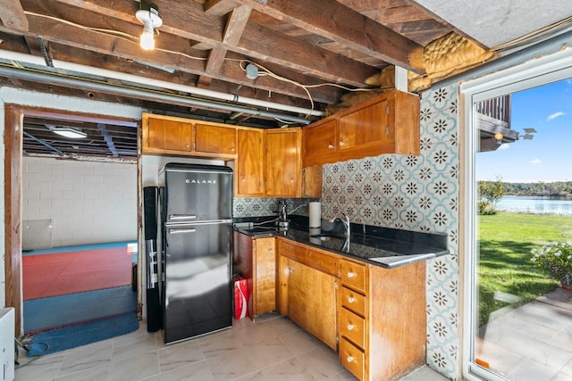 kitchen featuring black refrigerator, a water view, dark stone counters, and sink