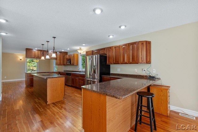 kitchen with kitchen peninsula, appliances with stainless steel finishes, light wood-type flooring, a center island, and hanging light fixtures