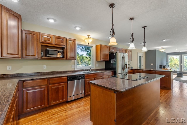 kitchen with pendant lighting, light hardwood / wood-style flooring, a textured ceiling, a kitchen island, and stainless steel appliances