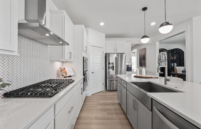 kitchen with wall chimney exhaust hood, hanging light fixtures, backsplash, white cabinets, and appliances with stainless steel finishes