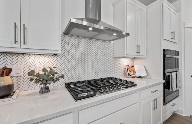 kitchen with decorative backsplash, double oven, wall chimney range hood, white cabinets, and stainless steel gas stovetop