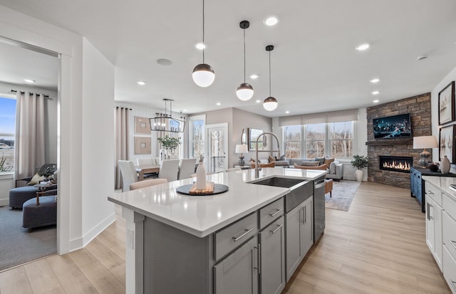 kitchen featuring stainless steel dishwasher, a kitchen island with sink, sink, a stone fireplace, and hanging light fixtures