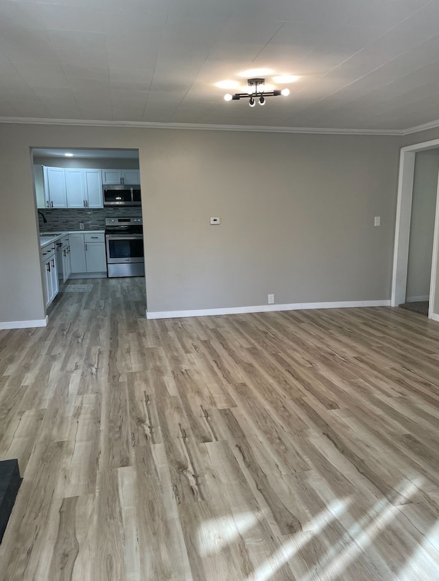 unfurnished living room with sink, ornamental molding, and light wood-type flooring