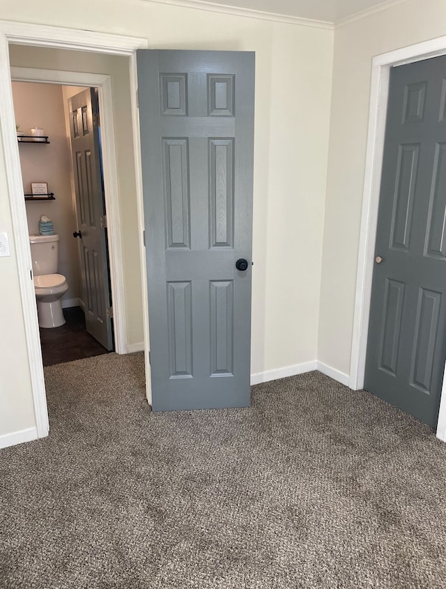 unfurnished bedroom with crown molding, ensuite bathroom, and dark colored carpet