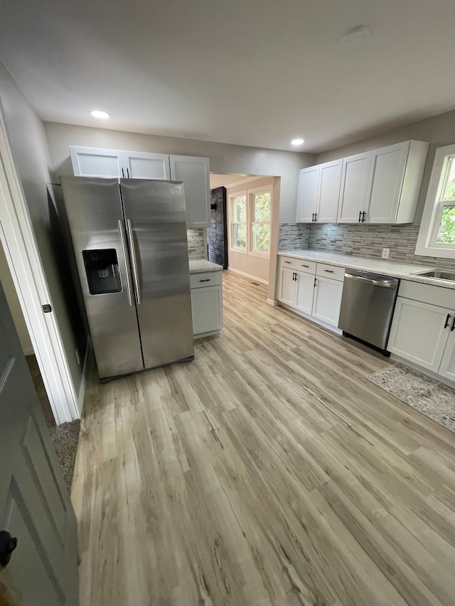 kitchen with backsplash, appliances with stainless steel finishes, light wood-type flooring, and white cabinets