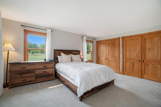 bedroom with light carpet, two closets, and multiple windows