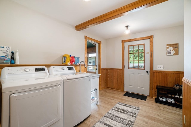 laundry room with light wood-type flooring, wooden walls, and washing machine and clothes dryer