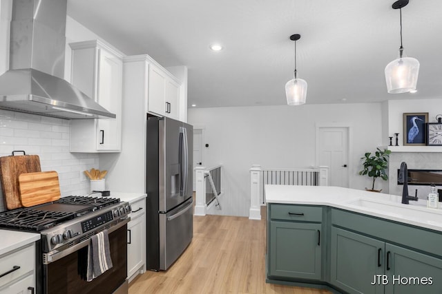 kitchen with appliances with stainless steel finishes, sink, wall chimney range hood, light hardwood / wood-style floors, and green cabinets