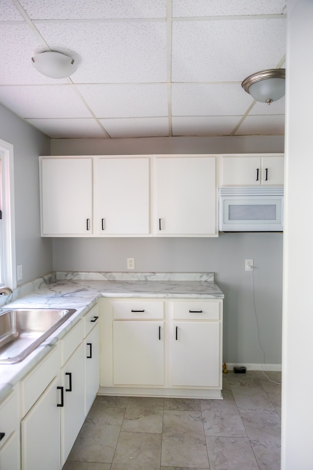 kitchen with white cabinets, a drop ceiling, and sink