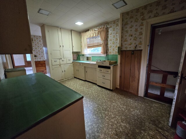 103 S Railroad St, Allen, MI 49227 - kitchen featuring wallpapered walls, cream cabinetry, a wainscoted wall, and light floors